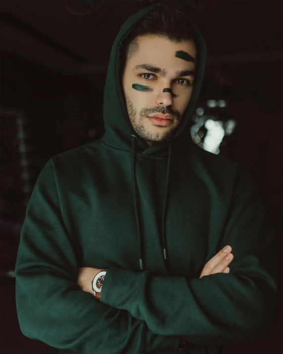 a young man wearing a hoodie standing with his arms crossed