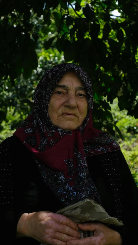 an old woman wearing a head scarf holds her hands close together