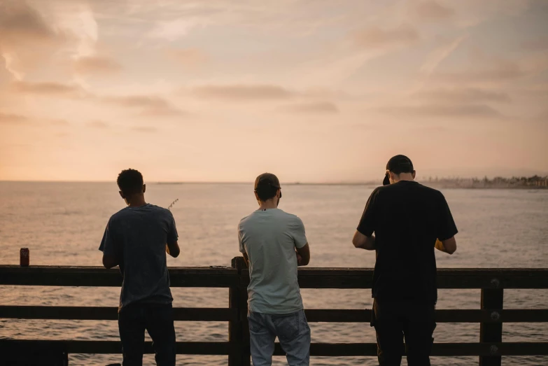 three men are standing at the end of a pier watching the water