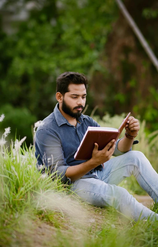 a man sitting down reading a book on top of green grass