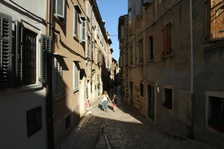 two people walk down a side alley in the sun