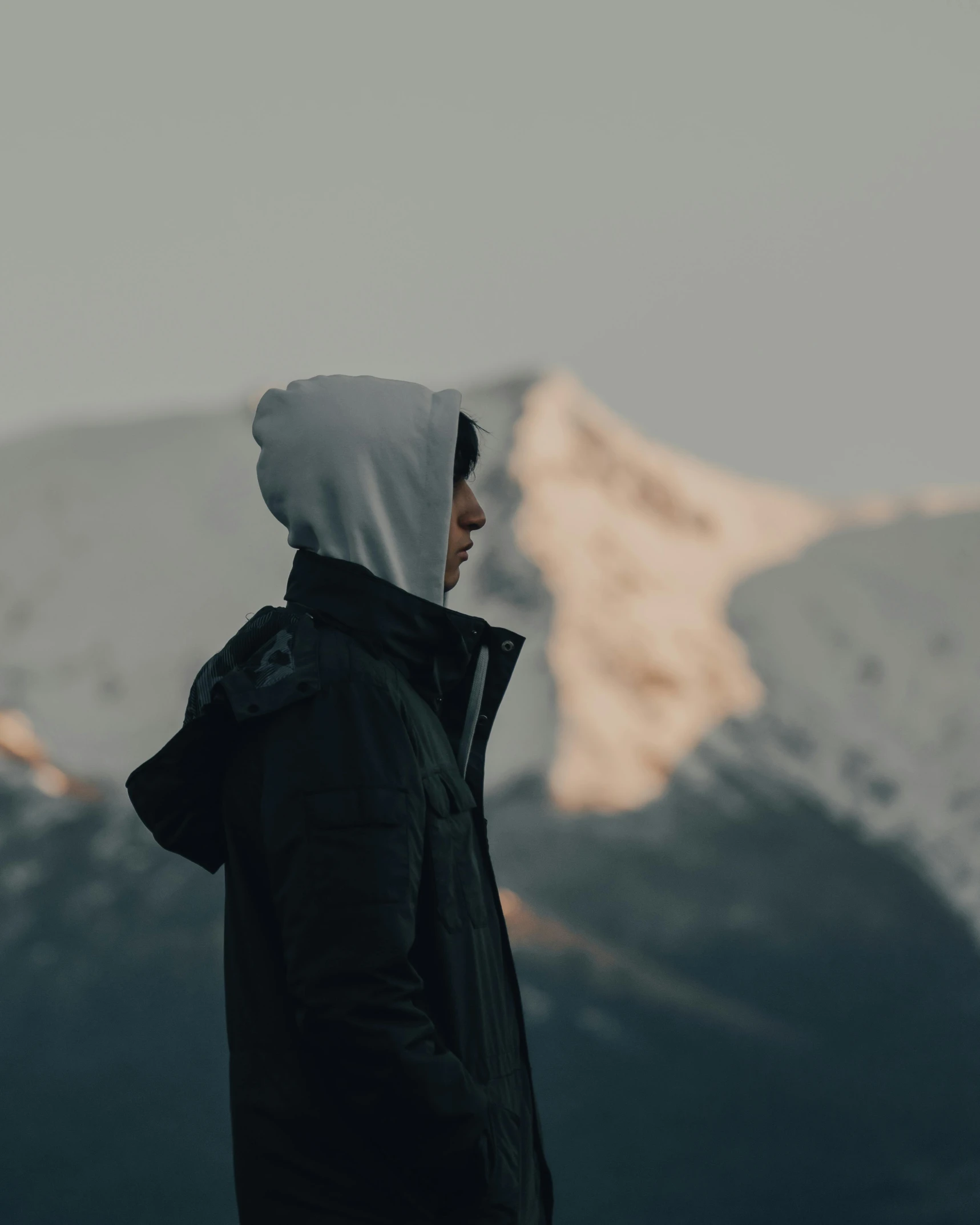 man in hooded jacket looking at mountains from top