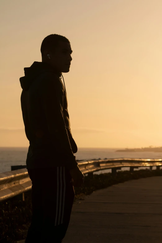 man in black tracksuit looking off in distance near a path next to the ocean