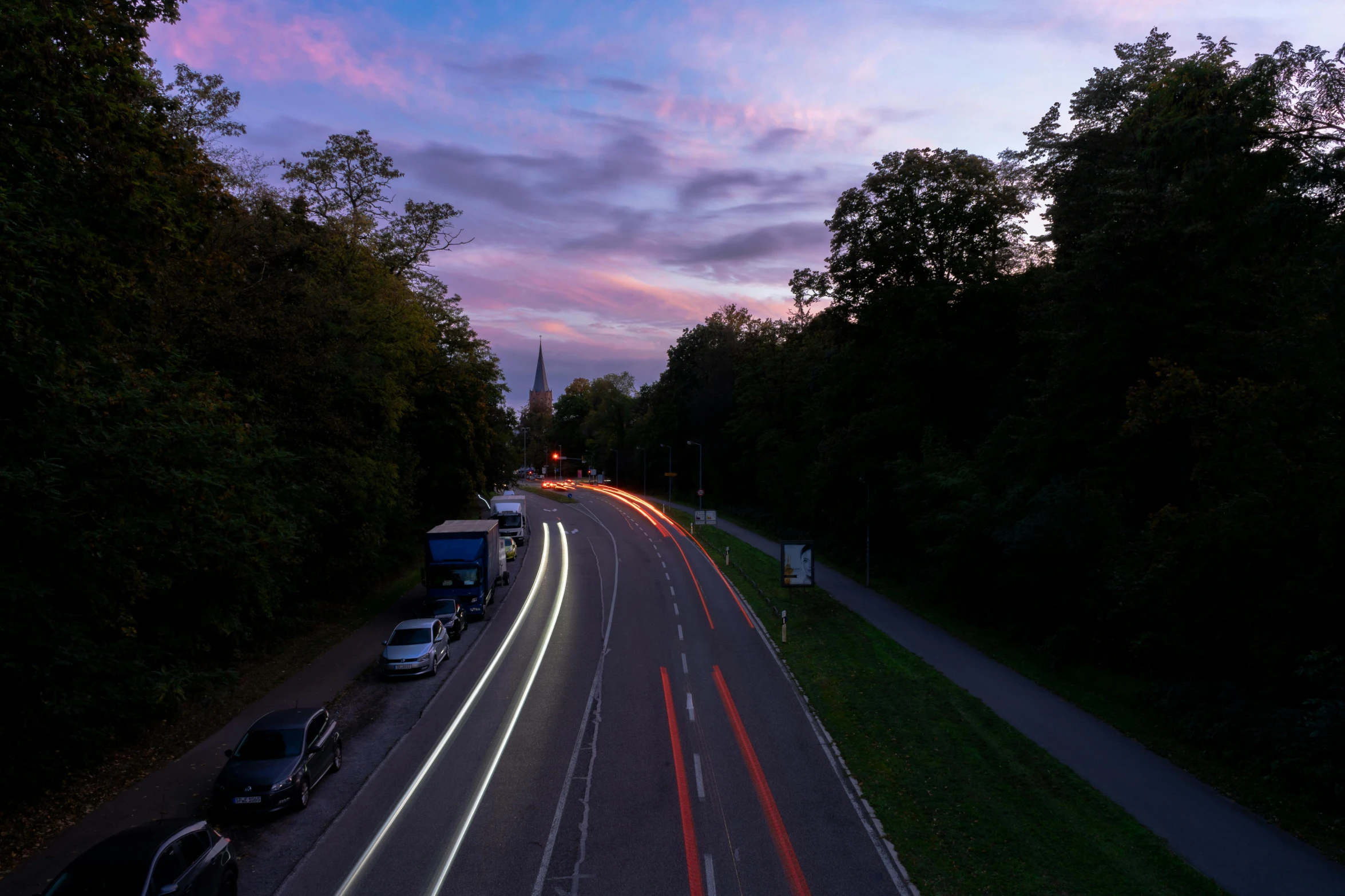 a road near the forest with a sky full of pink and purple clouds