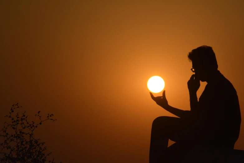 the sun is just above a horizon and behind a man sitting in a chair holding an object