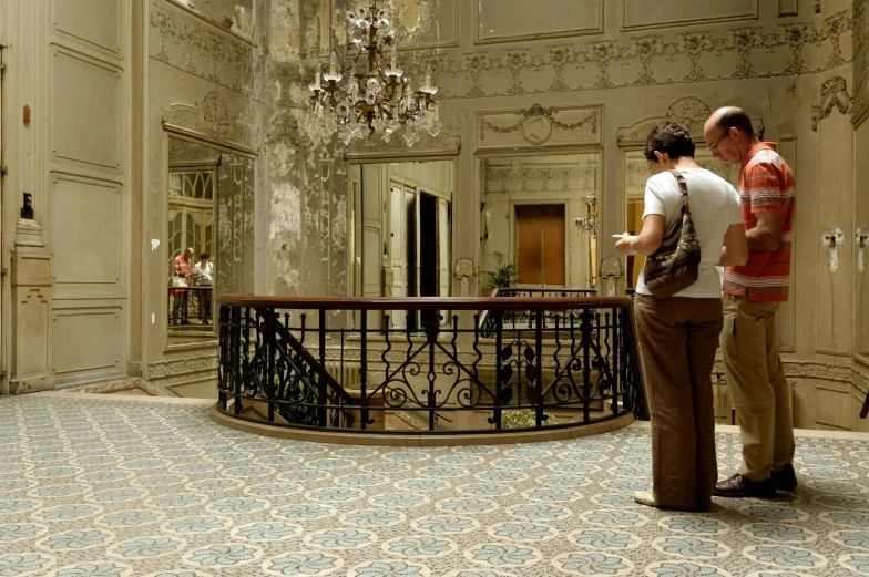 a couple talking while looking into a living room with an intricate ceiling