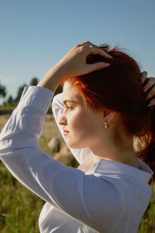 a woman standing in the grass holding her hair to her head
