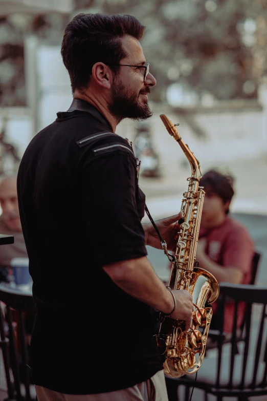 man with beard and glasses plays saxophone outdoors