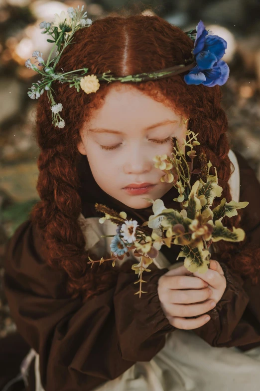 a young red - haired girl in a dress holds flowers, with her eyes closed