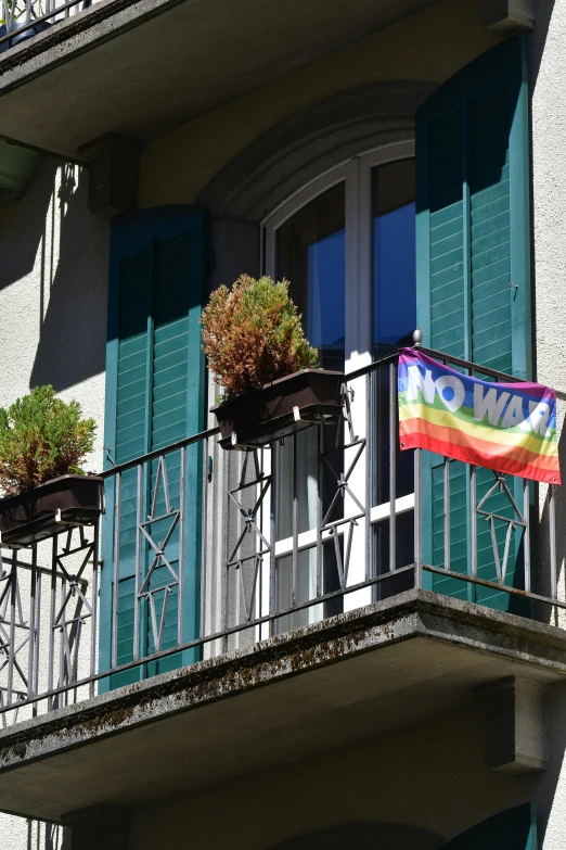 a window with blue shutters on two sides and a rainbow flag attached to the second