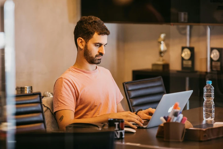 a man using a laptop at a desk in front of some glass