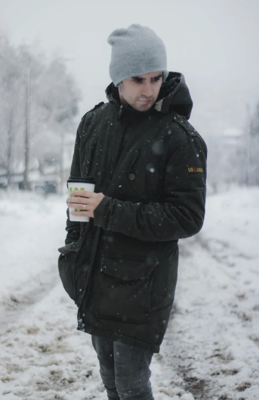 a man standing in the snow holding a cup of coffee