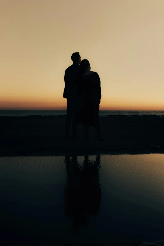 two people standing together at the beach hugging and kissing