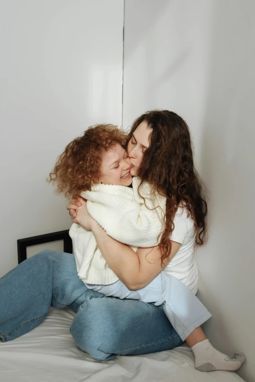 two women sitting on a bed while hugging each other