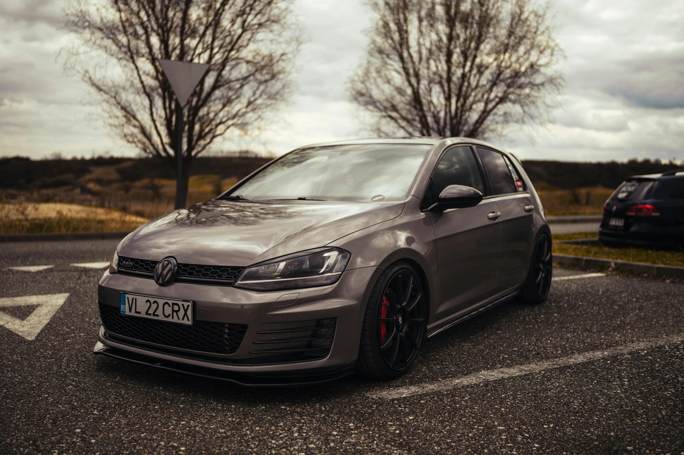 a grey volkswagen parked in a parking lot next to a forest