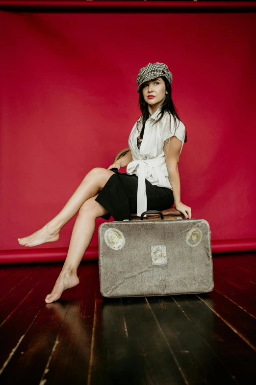 a woman in a hat sits with a piece of luggage