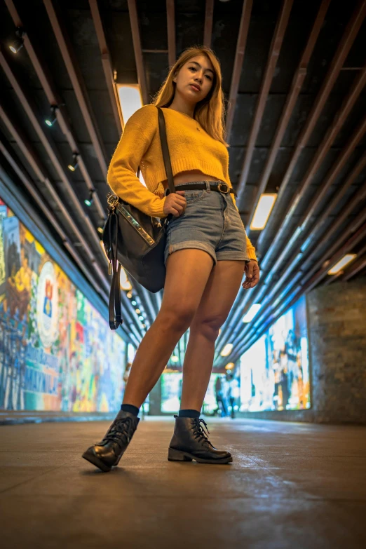 a woman with yellow sweater and blue shorts is standing in an underpass
