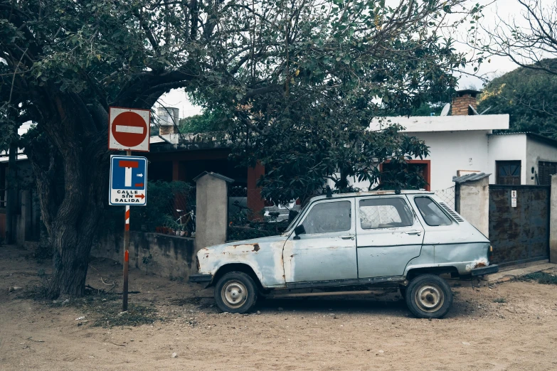 an old car sits on dirt near a street sign
