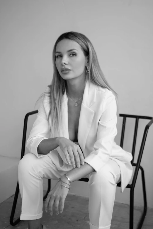 a woman with white suit sits on a chair