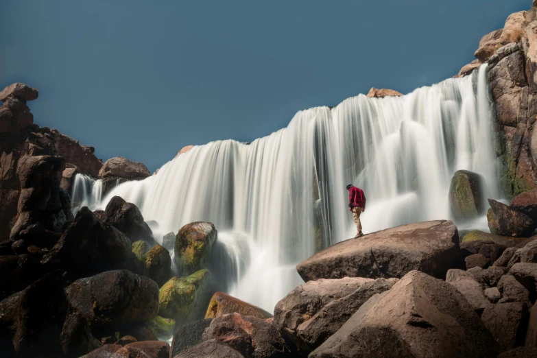 man with red umbrella standing next to waterfall