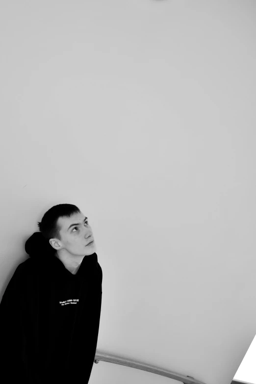 a young man in black sweatshirt leaning against wall