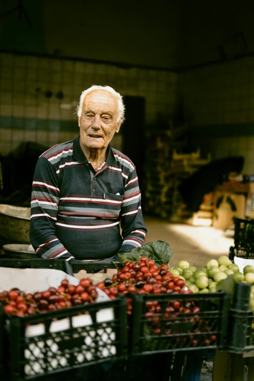 an older man sitting at a fruit stand with many fruits