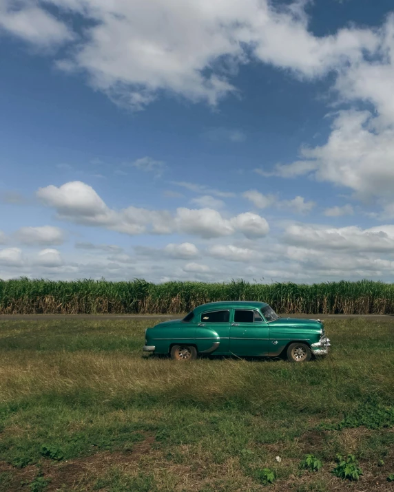 a green car is parked near a cornfield