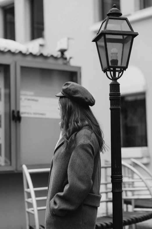 a woman standing on the sidewalk next to a street lamp