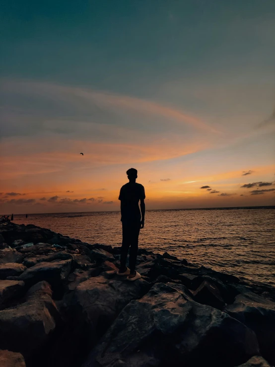 a man standing on a rocky shore at sunset