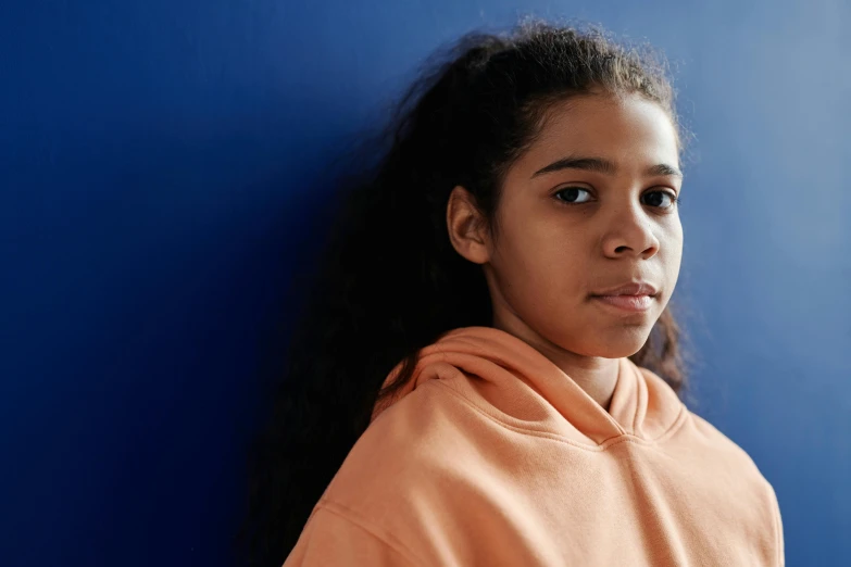 a woman in orange hooded sweatshirt leaning against a blue wall