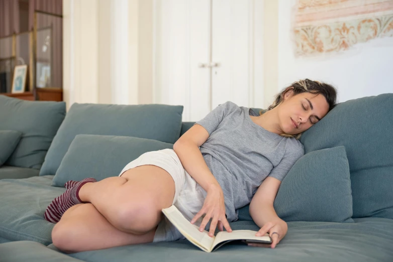 the girl is lying down on the couch reading a book