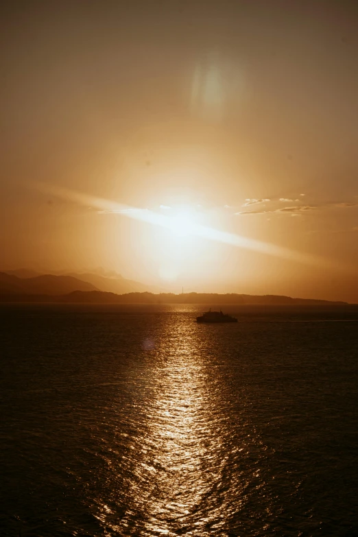 a ship sits in the distance of a vast body of water with the sun rising behind it