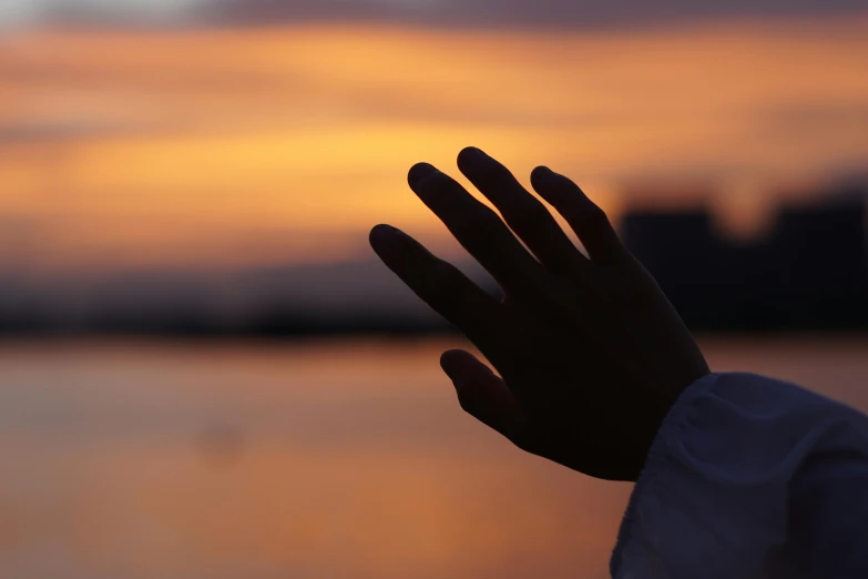 hand up at sunset with a blurry view of water