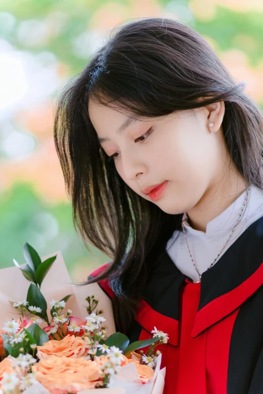 a girl wearing a graduation robe holds a bouquet