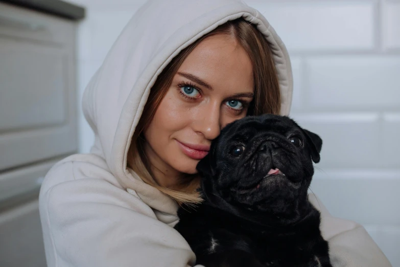a woman in a hooded hood holding a black pug