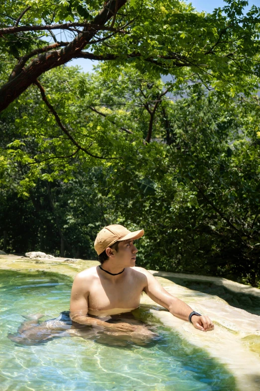 man with hat relaxing in natural pool surrounded by trees