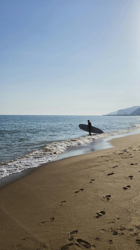 a lone person walks on the sand at the beach holding a surfboard