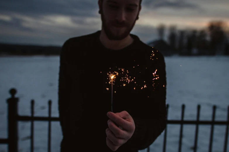 man holding up a sparkler in front of a frozen lake