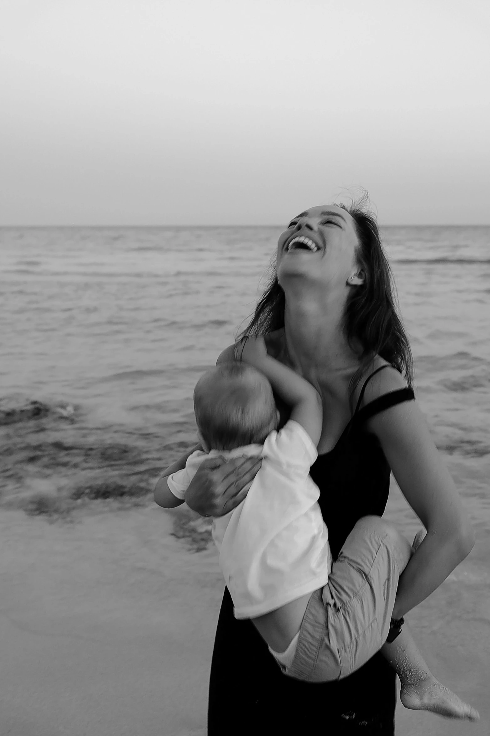 a woman holding a baby by the beach smiling