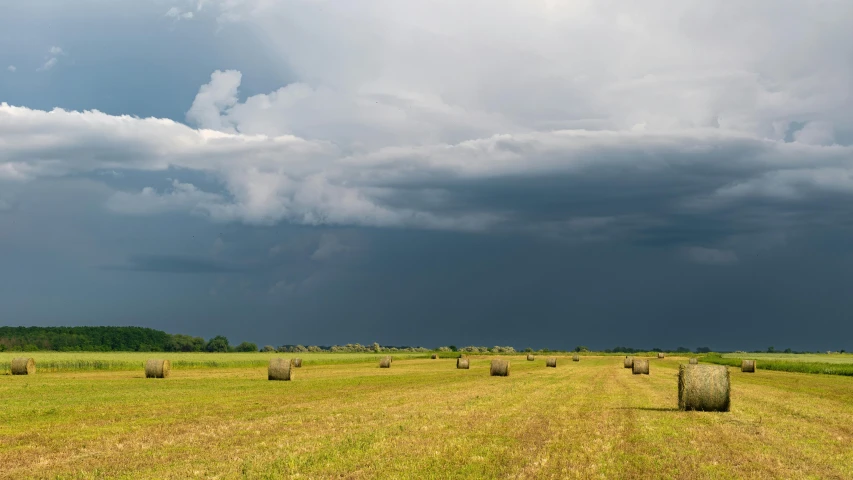 the big field is filled with hay bales under storm clouds