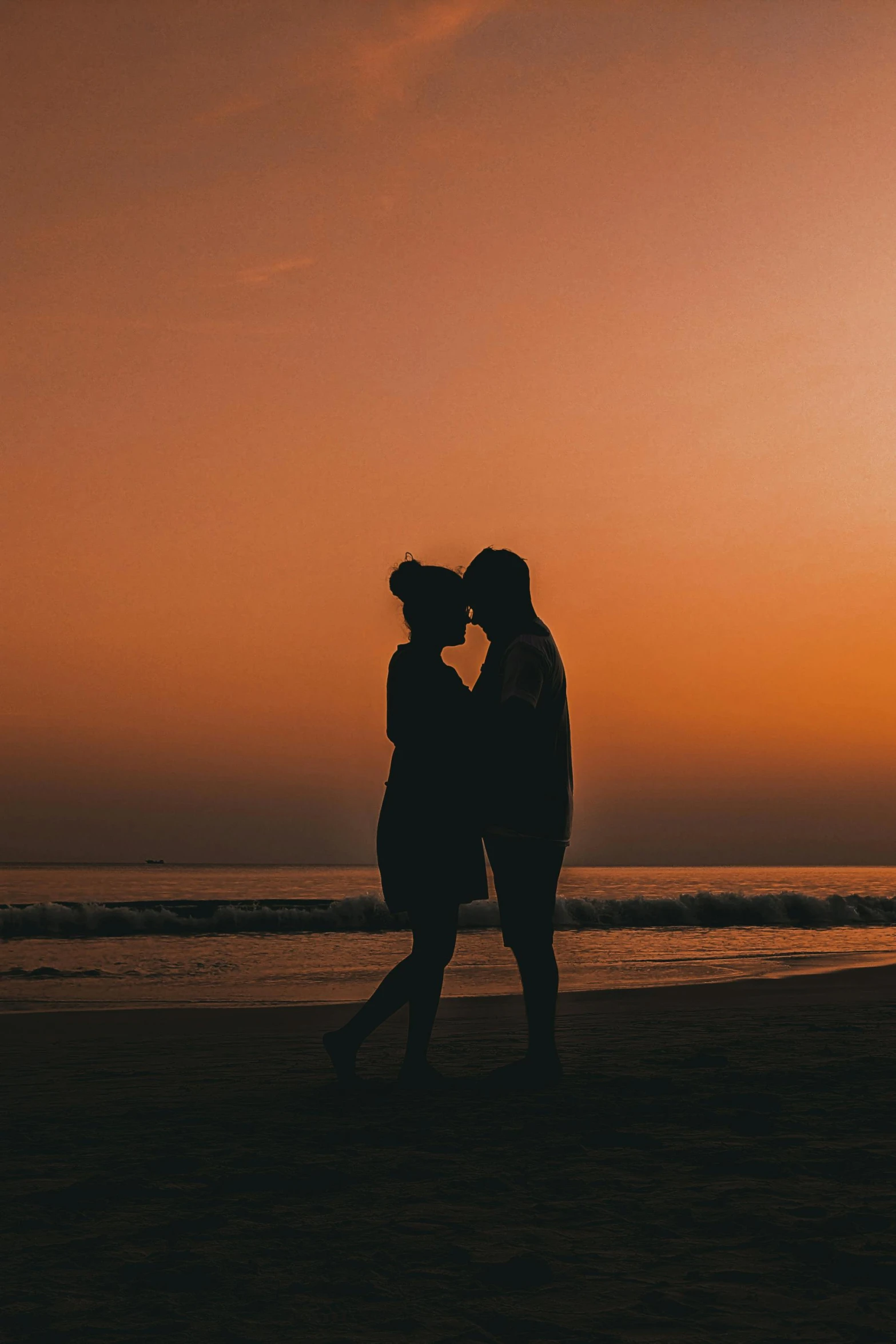 a man and woman are kissing on the beach at sunset