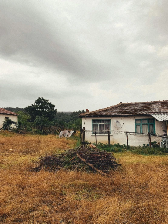 a dilapidated white house sitting in a field with trees and grass around it