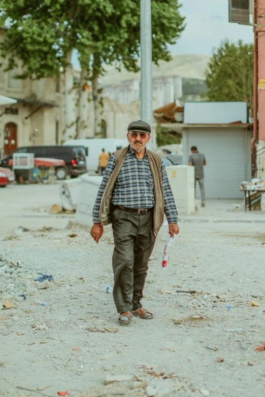 an old man in a hat and vest holding on to a street pole