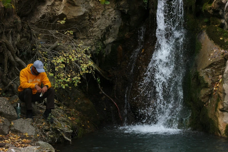 a man sitting by a small waterfall with a dog