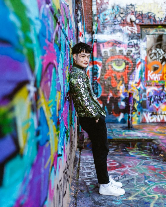 a boy stands against the side of a wall with graffiti