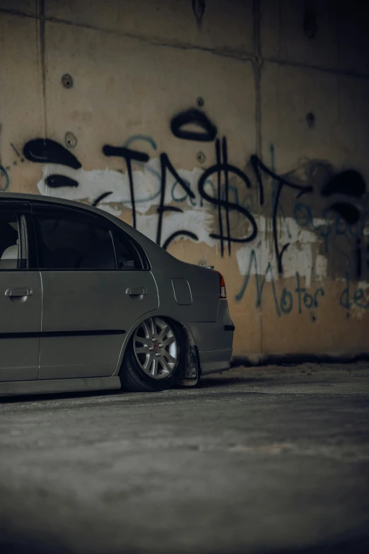 grey car parked in front of a wall with graffiti on it