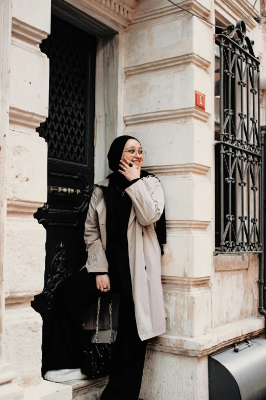 a woman with her hand under her chin leaning up against the corner of a building