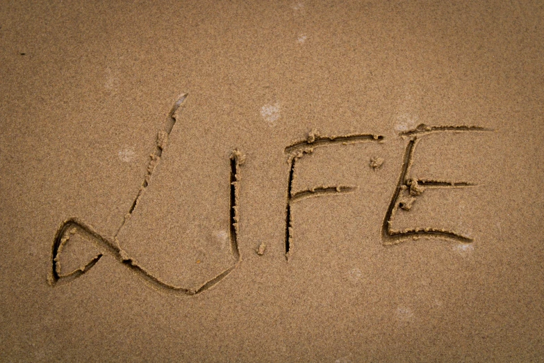 a close up of the word life written in sand