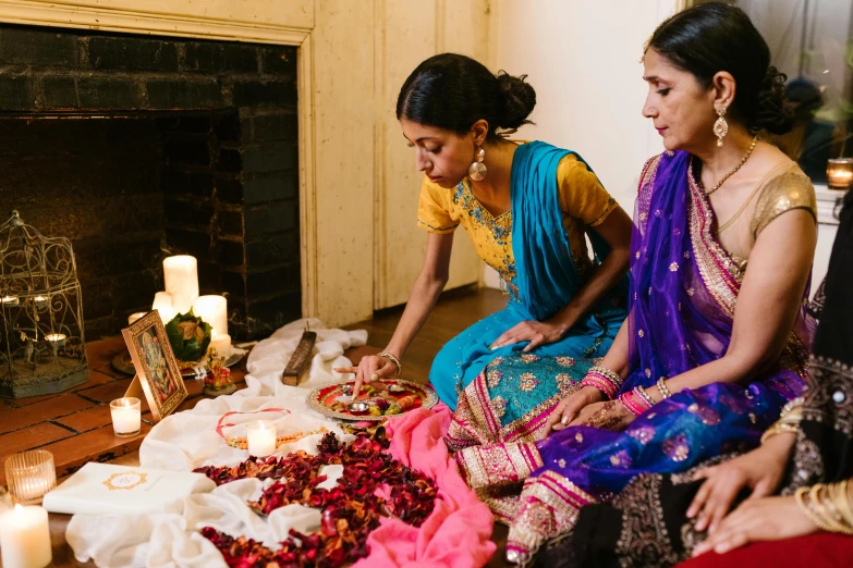 three women in saris are sitting on a floor and a fire place