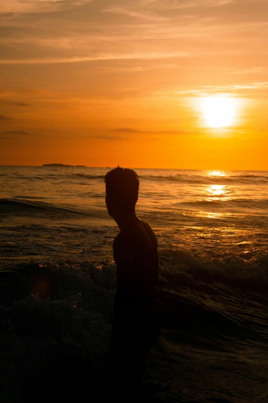 a silhouette of a man holding his surfboard while walking along the beach